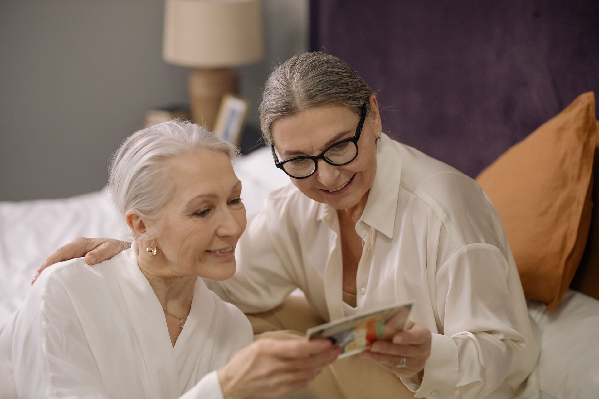 Two senior women enjoy a moment together reminiscing with old photographs indoors.