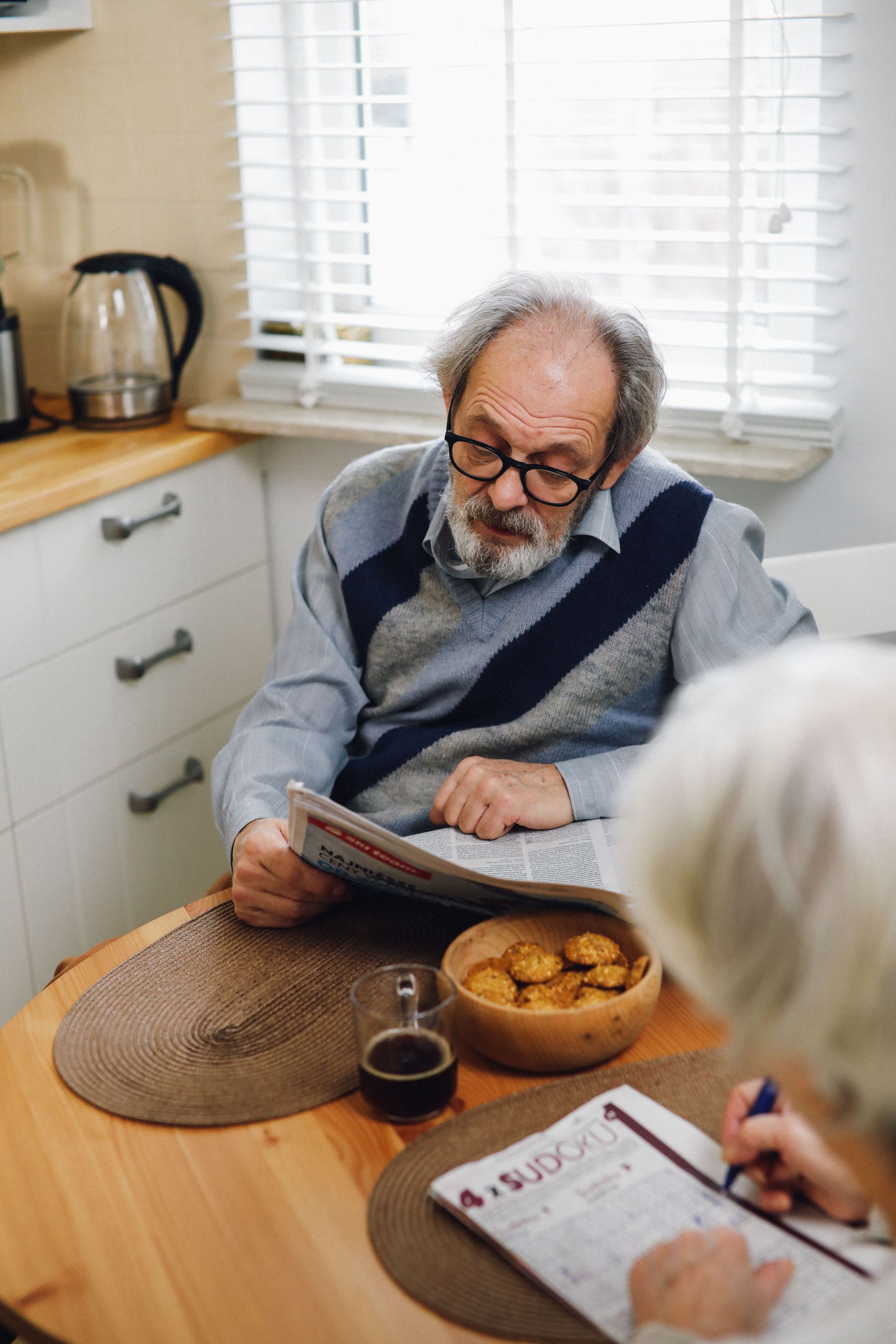 Elderly couple reading and enjoying a peaceful morning with coffee and cake.